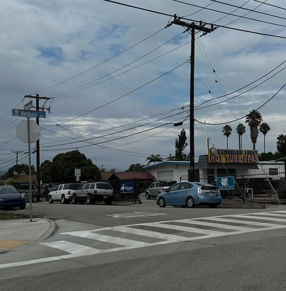 Street corner with parked cars, power lines, and cloudy sky.